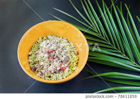 oatmeal with nuts and dried fruits in yellow bowl on black table near green palm leaf. Perfect whole grain breakfast as organic food. oatmeal with nuts and dried fruits in yellow bowl on black table near green palm leaf. Perfect whole grain breakfast as organic food. 78611859