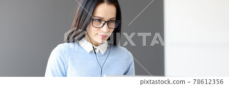 Young woman in headphones looking at laptop screen Young woman in headphones looking at laptop screen 78612356