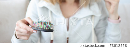 Young woman holding hair and looking at comb in surprise Young woman holding hair and looking at comb in surprise 78612358
