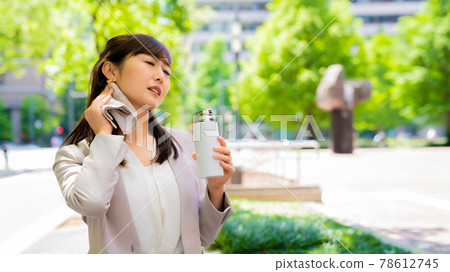 A business woman who rehydrates while wiping sweat outside 78612745