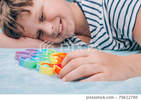 Smiling boy playing with rainbow pop it fidget toy. Push bubble fidget sensory toy - washable and reusable stress relief toy. Antistress toy for child with special needs. Mental health concept Smiling boy playing with rainbow pop it fidget toy. Push bubble fidget sensory toy - washable and reusable stress relief toy. Antistress toy for child with special needs. Mental health concept 78612780