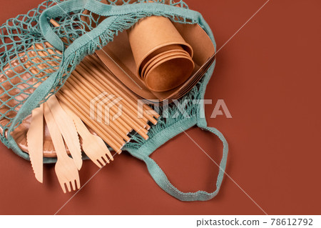 Kraft paper food cups and containers with wooden cutlery in blue cotton net bag on brown background with copy space for text. Eco-friendly tableware. Street food take away paper packaging 78612792