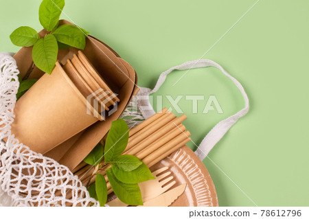 Close up view of eco-friendly tableware - kraft paper food cups and containers with wooden cutlery in white cotton net bag on light green background with copy space. Street food paper packaging 78612796
