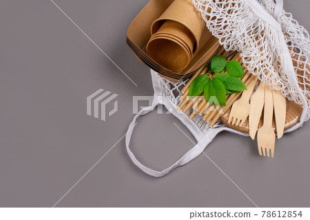 Close up of eco-friendly tableware - kraft paper food cups and containers with wooden cutlery in white cotton net bag on light gray background with copy space. Street food take away paper packaging 78612854