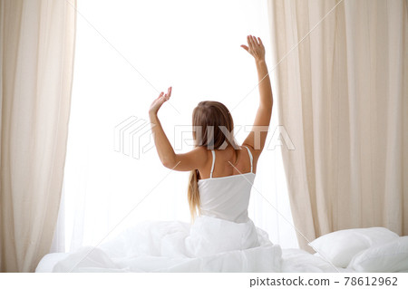 Woman stretching in bed after wake up, back view, entering a day happy and relaxed after good night sleep. Sweet dreams, good morning, new day, weekend, holidays concept 78612962