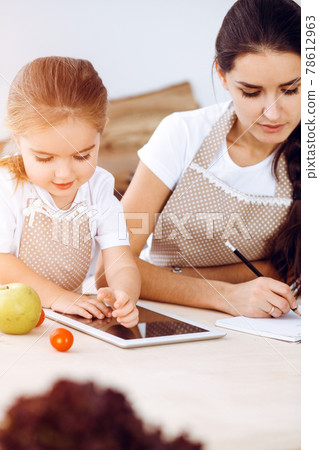 Happy woman and her daughter are searching for new recipes for a family feasting, sunny kitchen. Christmas, New year, Thanksgiving, Anniversary, Mothers Day. Healthy meal cooking concept 78612963