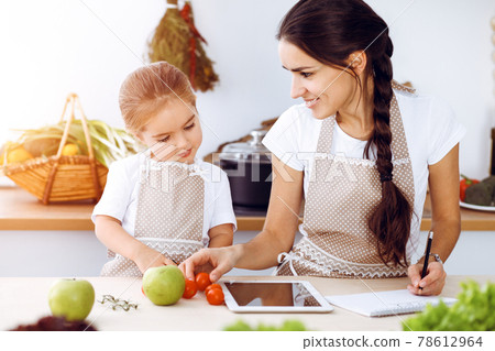 Happy woman and her daughter are searching for new recipes for a family feasting, sunny kitchen. Christmas, New year, Thanksgiving, Anniversary, Mothers Day. Healthy meal cooking concept 78612964