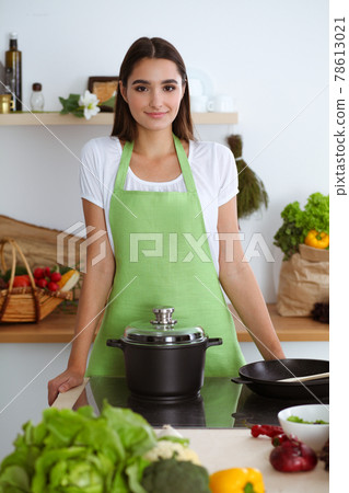 An attractive young dark-haired woman preparing soup by new keto recipe while standing and smiling in the kitchen. Cooking and householding concepts 78613021