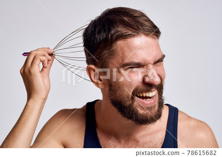 man with a massager for the head and in a blue t-shirt on a light background relaxing beard emotions man with a massager for the head and in a blue t-shirt on a light background relaxing beard emotions 78615682