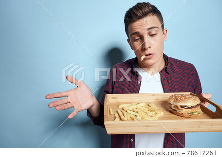 Man with wooden pallet fast food french fries hamburger hunger diet food blue background Man with wooden pallet fast food french fries hamburger hunger diet food blue background 78617261
