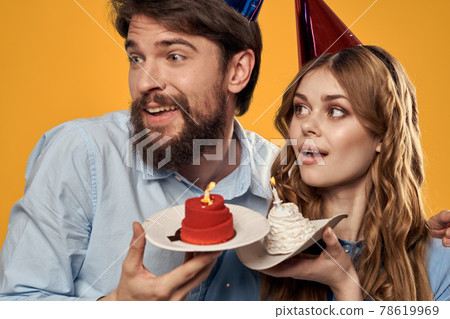 Birthday party man and woman in a cap with a cake on a yellow background cropped view Birthday party man and woman in a cap with a cake on a yellow background cropped view 78619969