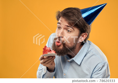 Man with cake on yellow background birthday party hat cropped view 78620333