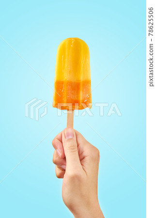 Yellow frozen fruit ice cream popsicle in hand on blue background 78625506