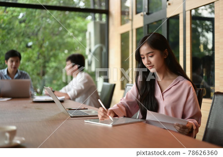 Young businesswoman at modern startup office working on tablet, blured team in meeting background. Young businesswoman at modern startup office working on tablet, blured team in meeting background. 78626360