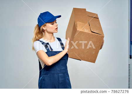 A woman in a working uniform with a box in the hands of a delivery service delivery service light background A woman in a working uniform with a box in the hands of a delivery service delivery service light background 78627276