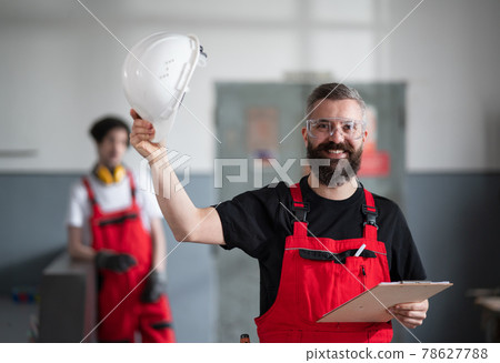 Portrait of cheerful worker with helmet and protective glasses indoors in factory looking at camera. Portrait of cheerful worker with helmet and protective glasses indoors in factory looking at camera. 78627788