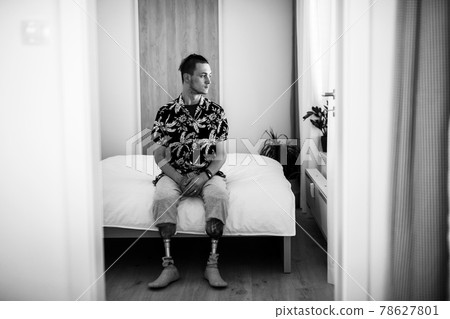 Black and white portrait of disabled young man sitting in bed indoors at home, leg prosthetic concept. Black and white portrait of disabled young man sitting in bed indoors at home, leg prosthetic concept. 78627801