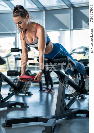 Sporty girl doing hyperextension with weight plate at gym 78627968