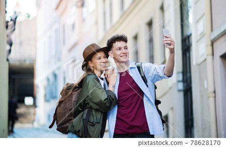 Young couple travelers with smartphone sightseeing in city on holiday, taking selfie. 78628170
