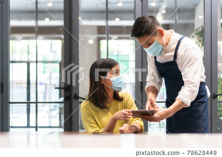 Asian Waiter wearing protective face mask taking order from Female customer Asian Waiter wearing protective face mask taking order from Female customer 78628449
