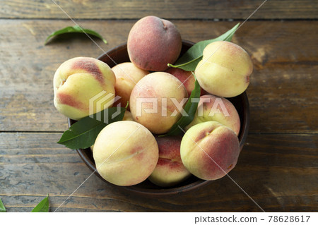 Ripe peaches with leaves in a clay bowl on a wooden table. Ripe peaches with leaves in a clay bowl on a wooden table. 78628617