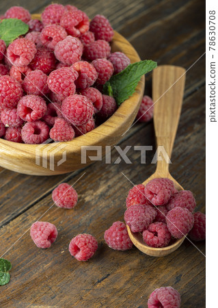 Fresh raspberries in a wooden plate with leaves. The berries are scattered on a wooden table. 78630708