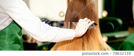 Hairdresser combing long hair of client Hairdresser combing long hair of client 78632139
