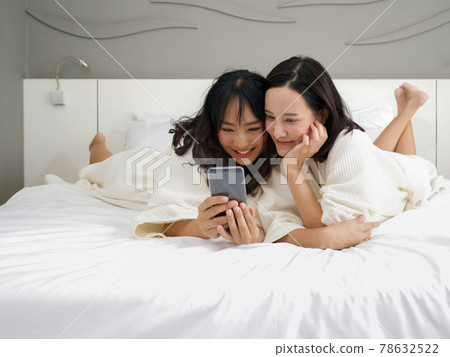 Two Asian women in bathrobe take a selfie with a mobile phone while lying in bed. Two Asian women in bathrobe take a selfie with a mobile phone while lying in bed. 78632522