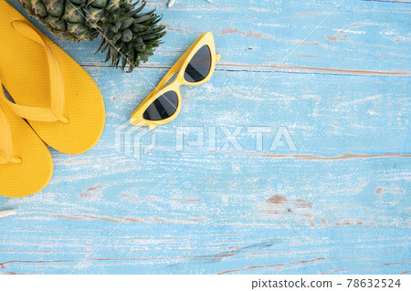 top view of yellow slippers pineapple and sunglasses on blue wooden background,Flat lay of summer and travel equipment with copy space,Summer vacation and travel concept 78632524