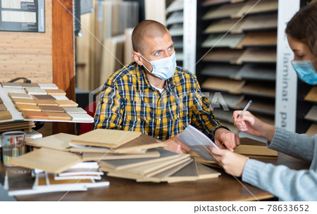 Seller in mask consulting customer about purchase of laminate flooring 78633652