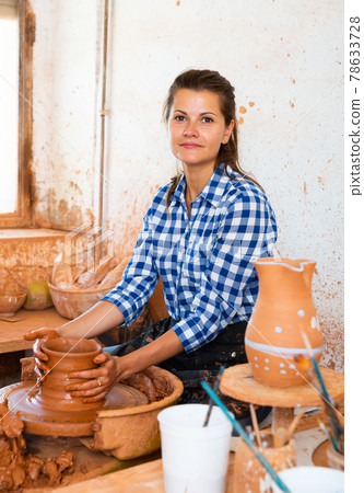 Portrait of adult female potter working with clay on pottery wheel in atelier 78633728