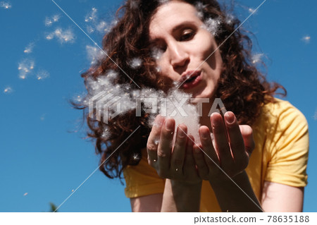 Girl blows poplar fluff off her hands. Fluff flies in different directions Girl blows poplar fluff off her hands. Fluff flies in different directions 78635188