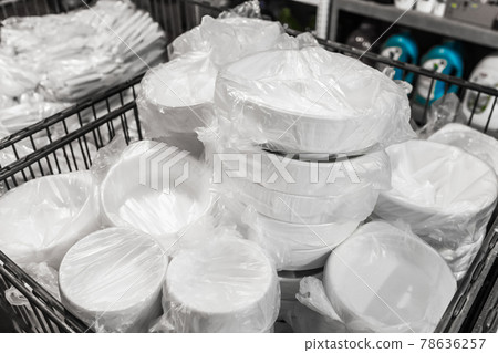 A set of white disposable plastic tableware in cellophane packaging in a store A set of white disposable plastic tableware in cellophane packaging in a store 78636257