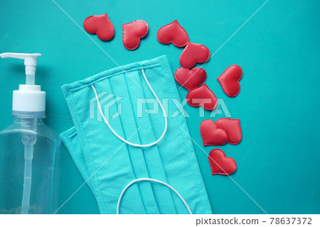 Surgical masks with heart shape and hand sanitizer on color background  78637372
