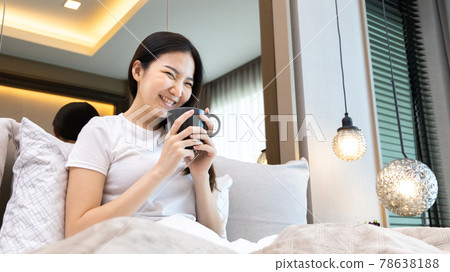 Asian woman sipping coffee on a luxurious bed in a manicured bedroom, After waking up have to drink coffee to refresh and get ready for a new day, relaxation, wake up morning, Hot coffee. Asian woman sipping coffee on a luxurious bed in a manicured bedroom, After waking up have to drink coffee to refresh and get ready for a new day, relaxation, wake up morning, Hot coffee. 78638188