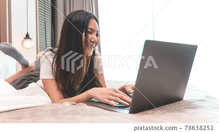 Asian woman uses laptop on bed in modern bedroom at home after she wakes up in the morning, Entertaining or relaxing using laptop technology, Wake-up activities, Happy lifestyle. Asian woman uses laptop on bed in modern bedroom at home after she wakes up in the morning, Entertaining or relaxing using laptop technology, Wake-up activities, Happy lifestyle. 78638251
