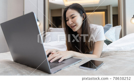 Asian woman uses laptop on bed in modern bedroom at home after she wakes up in the morning, Entertaining or relaxing using laptop technology, Wake-up activities, Happy lifestyle. Asian woman uses laptop on bed in modern bedroom at home after she wakes up in the morning, Entertaining or relaxing using laptop technology, Wake-up activities, Happy lifestyle. 78638252