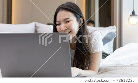 Asian woman uses laptop on bed in modern bedroom at home after she wakes up in the morning, Entertaining or relaxing using laptop technology, Wake-up activities, Happy lifestyle. 78638253