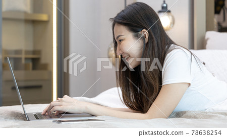 Asian woman uses laptop on bed in modern bedroom at home after she wakes up in the morning, Entertaining or relaxing using laptop technology, Wake-up activities, Happy lifestyle. 78638254