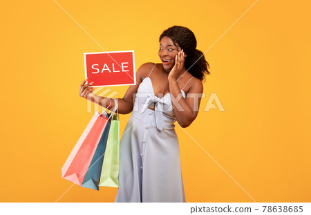 Pretty African American woman holding shopping bags and SALE sign, feeling excited over orange studio background 78638685