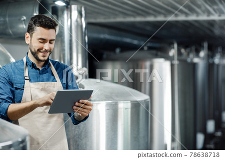 Young man work at beer factory. Brewer, industrial equipment and modern smart digital device at brewery Young man work at beer factory. Brewer, industrial equipment and modern smart digital device at brewery 78638718