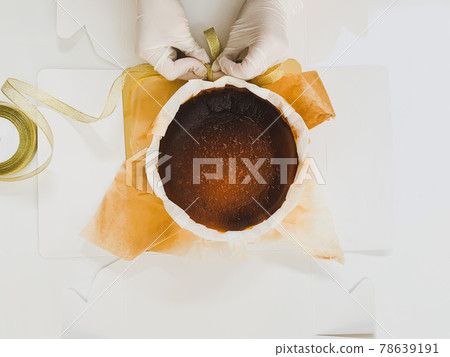 Female baker hand with glove packing basque burnt cheesecake cake with ribbon. Female baker hand with glove packing basque burnt cheesecake cake with ribbon. 78639191