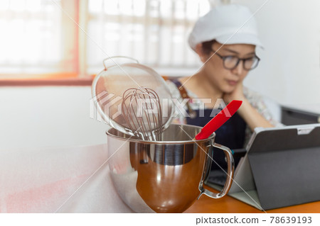 Selected focus of bakery equipment with woman baker working on laptop in background. Selected focus of bakery equipment with woman baker working on laptop in background. 78639193