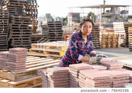 Female warehouse employee puts paving slabs on pallet Female warehouse employee puts paving slabs on pallet 78640386