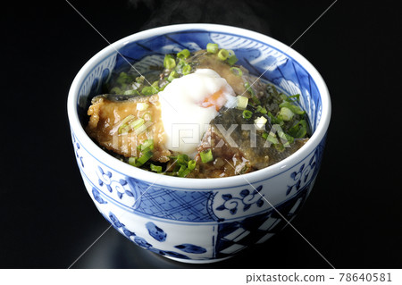 Photographed a hot yellowtail teriyaki rice bowl topped with hot balls and plenty of small onions on a black background 78640581