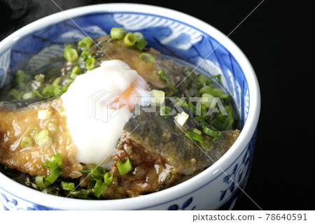 Photographed a hot yellowtail teriyaki rice bowl topped with hot balls and plenty of small onions on a black background 78640591