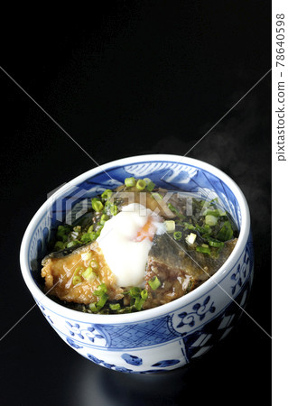 Photographed a hot yellowtail teriyaki rice bowl topped with hot balls and plenty of small onions on a black background 78640598