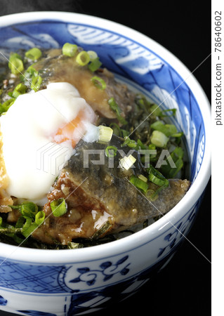 Photographed a hot yellowtail teriyaki rice bowl topped with hot balls and plenty of small onions on a black background 78640602