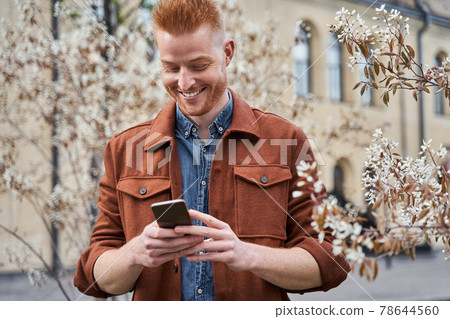 Man standing around the blossom trees and looking at his smartphone Man standing around the blossom trees and looking at his smartphone 78644560