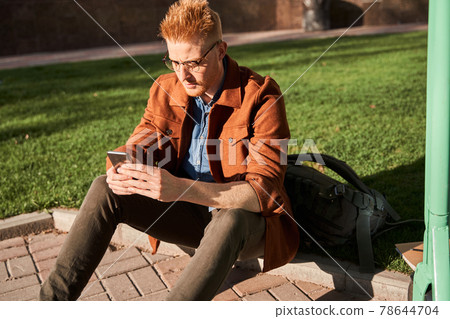 Man sitting at the street and holding mobile phone Man sitting at the street and holding mobile phone 78644704